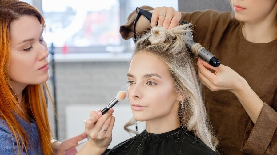 cosmetologists applying makeup and hair treatments to a client