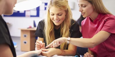 nail tech teacher assisting a student during a manicure