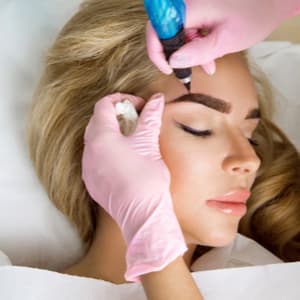 permanent makeup artist tattooing a woman's eyebrows