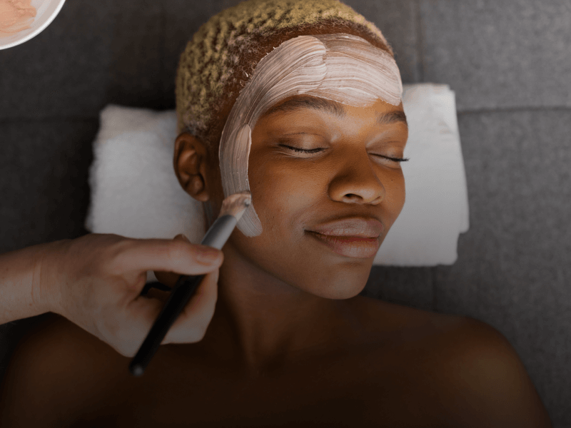 a person applying a facial treatment mask on a customer's face